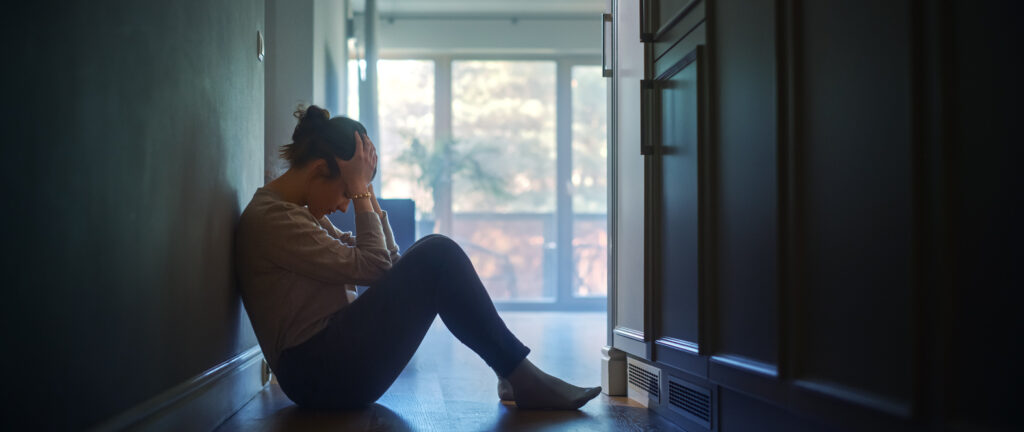 Sad Young Woman Sitting on the Floor In the Hallway of Her Home, Covering Face with Hands. Atmosphere of Depression, Trouble in Relationship, Death in the Family. Dramatic Bad News Moment