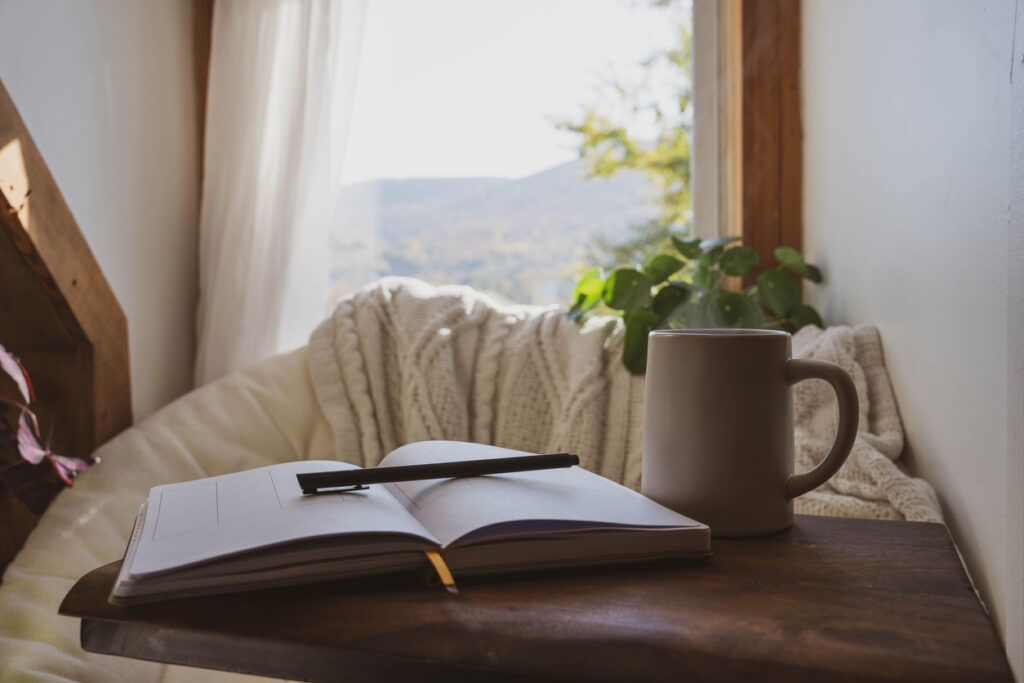 A cozy mental health break with an open journal, pen and coffee cup in front of a window