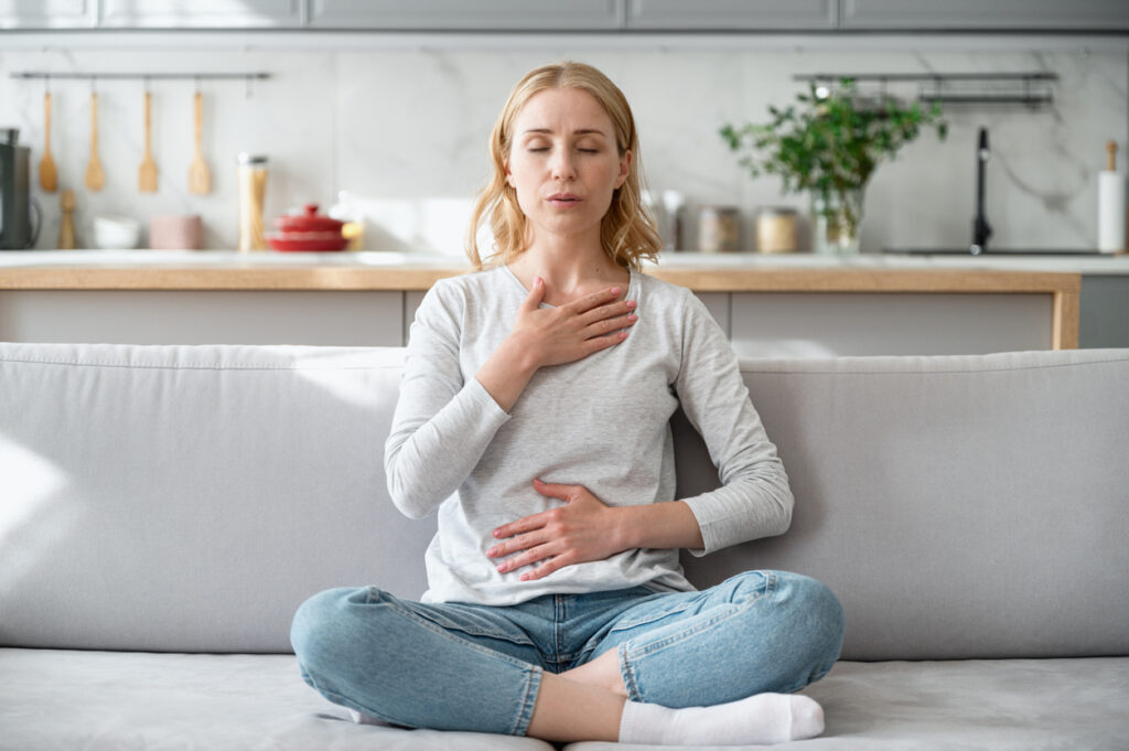 Woman Doing Calming Breathing Exercises Sat On A Sofa At Home