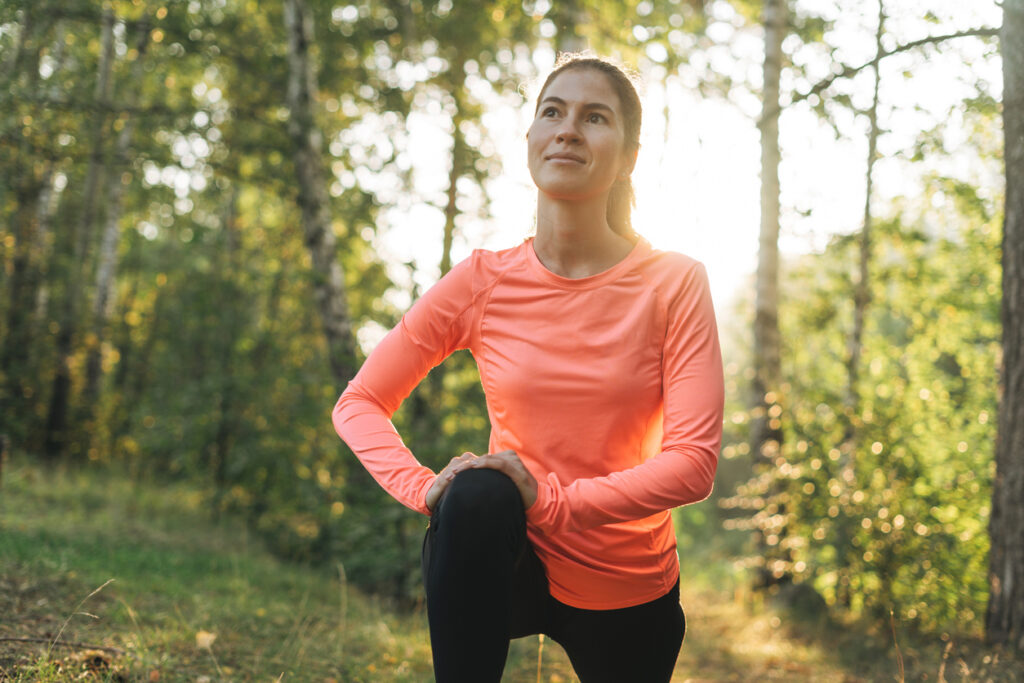 Brunette woman in sport clothes doing stretching in the forest at sunrise