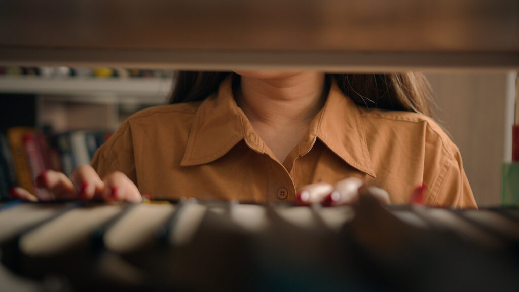 Close-up unrecognizable woman teacher girl student female customer bookworm browsing bookcase searching necessary book to read on bookshelf looking for literature in library search textbook books