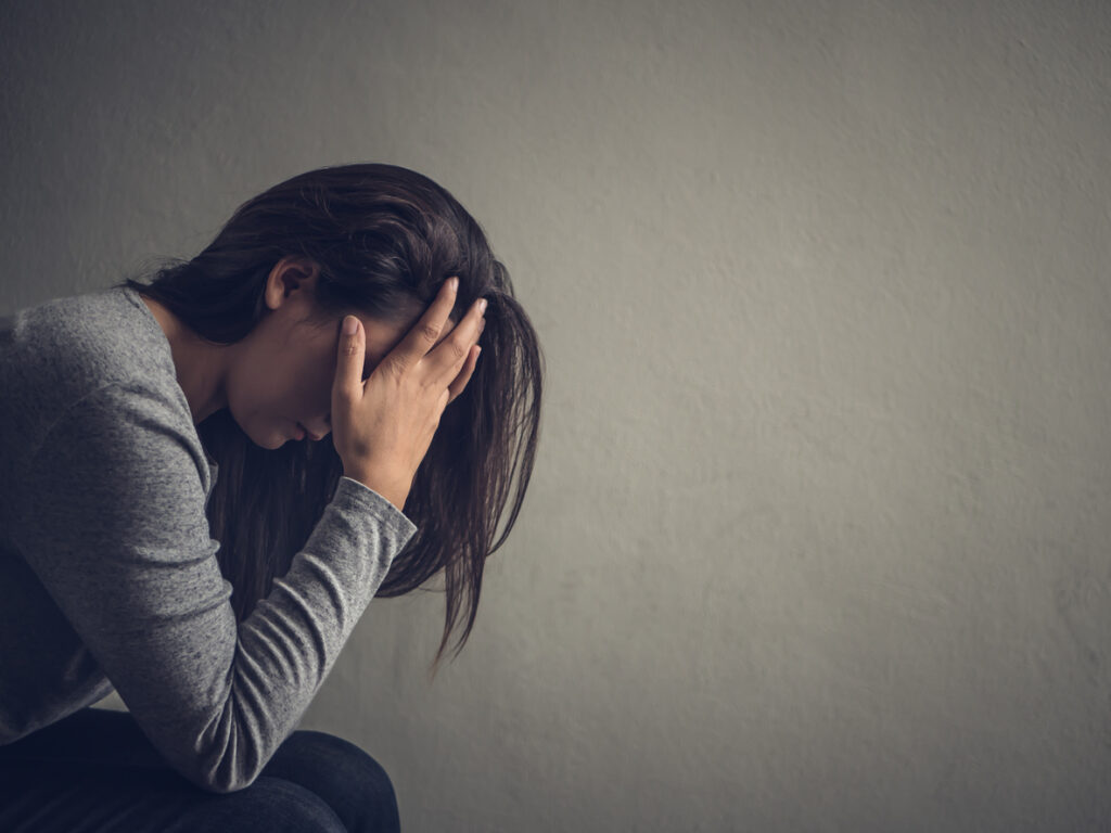 Stressed Woman Sitting On A Chair In A Dark Room At Home