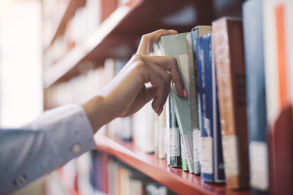 Woman at the library, she is searching books on the bookshelf and picking a textbook, hand close up