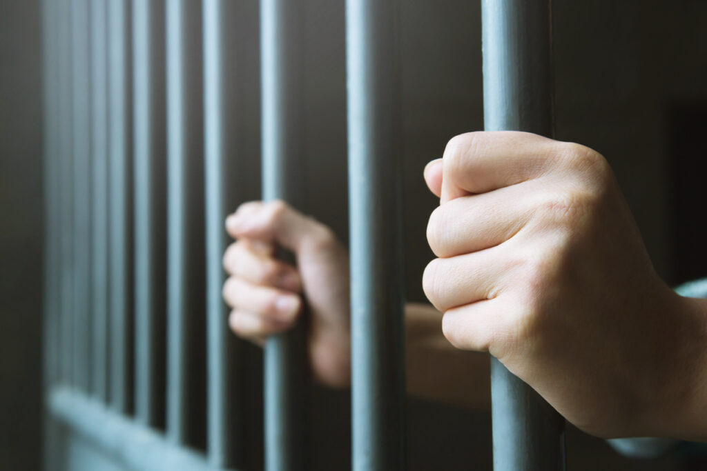 Hands of a man in prison holding jail bars