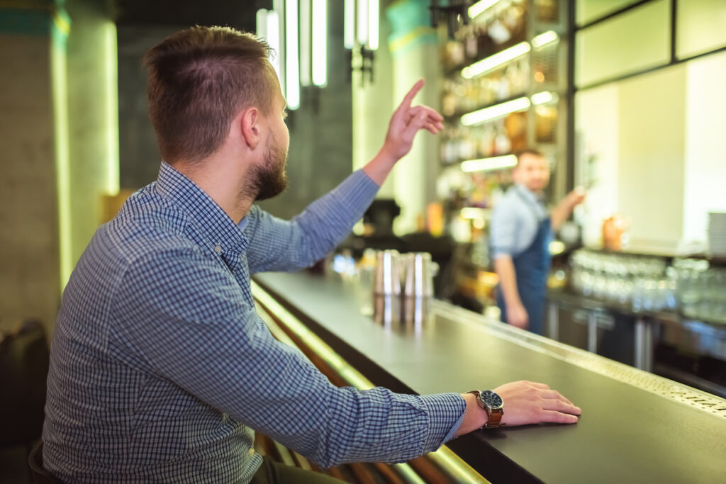 Male customer at a bar signalling the attention of a member of staff by raising his arm