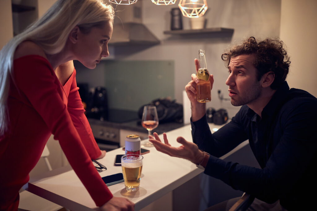 Angry wife arguing with her drunk husband in the kitchen with beer and glasses of wine on the kitchen counter